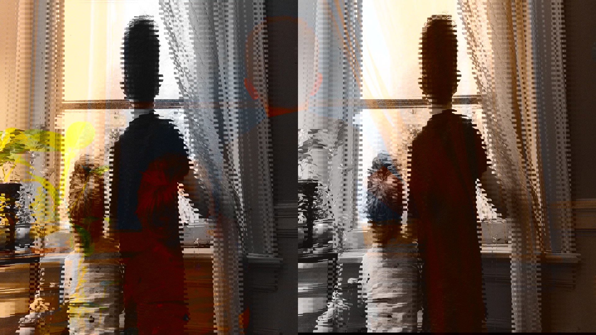 Två barn står och tittar ut i ett fönster